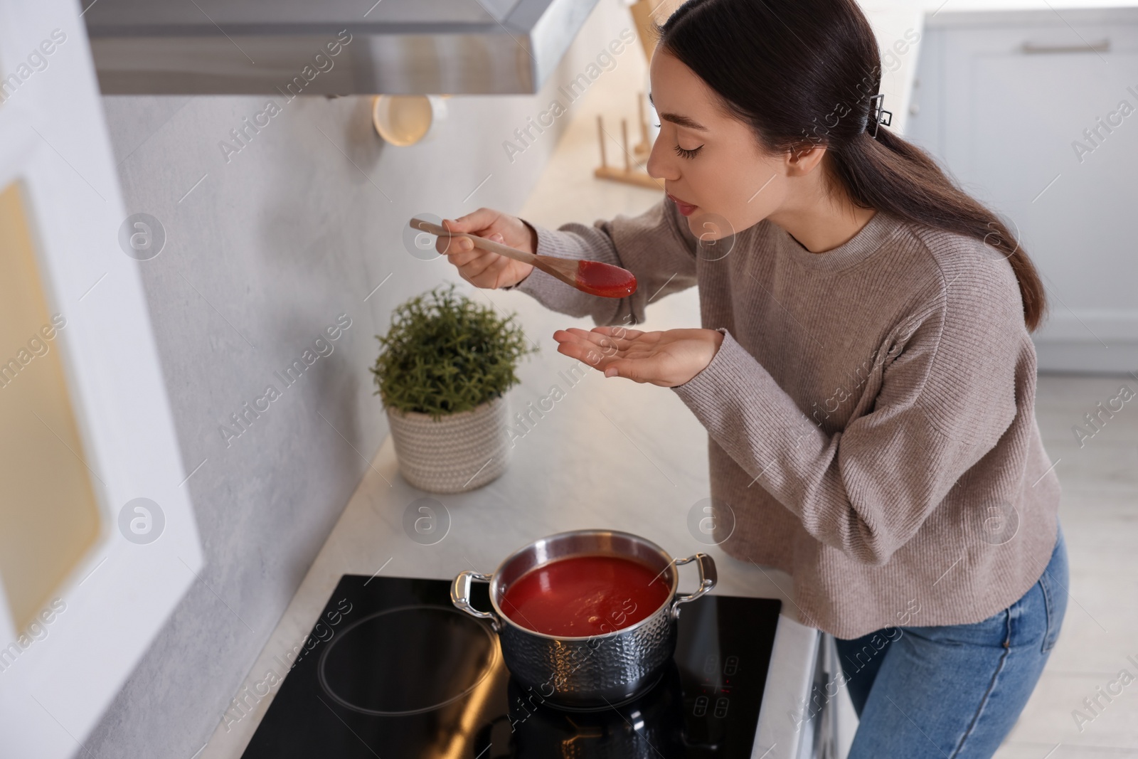 Photo of Beautiful woman with wooden spoon tasting tomato soup in kitchen, above view