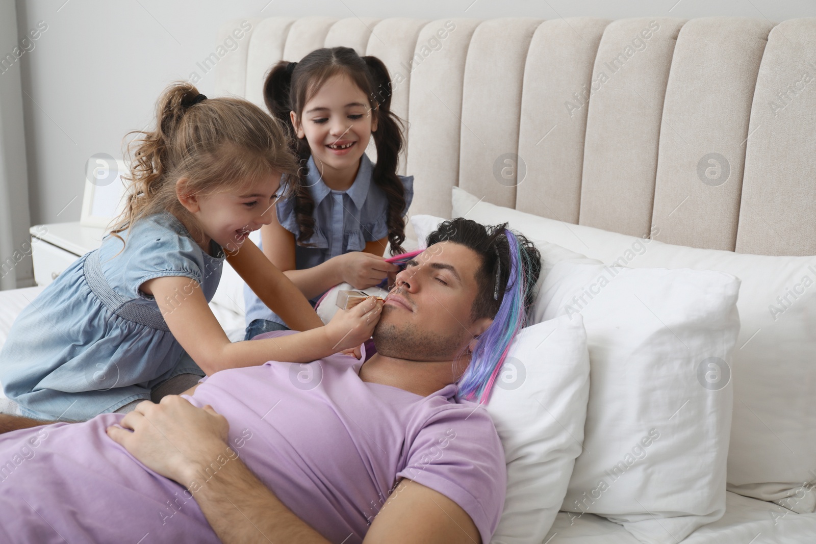 Photo of Cute little children painting face of their father while he sleeping in bed at home