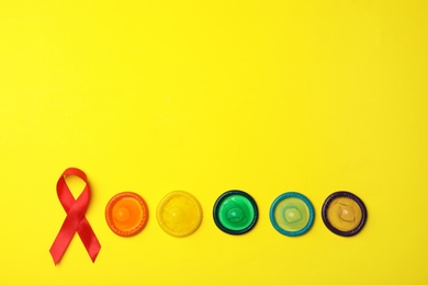 Photo of Flat lay composition with colorful condoms and red ribbon on yellow background, space for text. LGBT concept