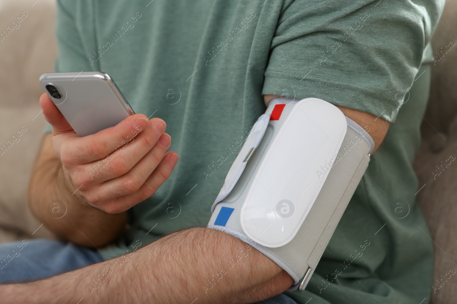 Photo of Man checking blood pressure with modern monitor and smartphone indoors, closeup