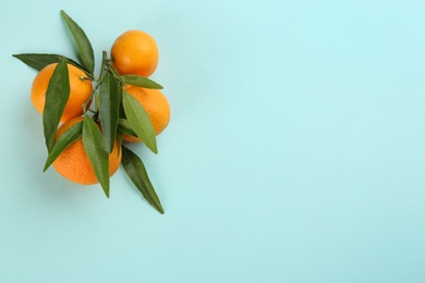 Photo of Fresh tangerines with green leaves on light blue background, flat lay. Space for text