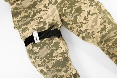 Photo of Soldier in military uniform with medical tourniquet on leg against white background, closeup