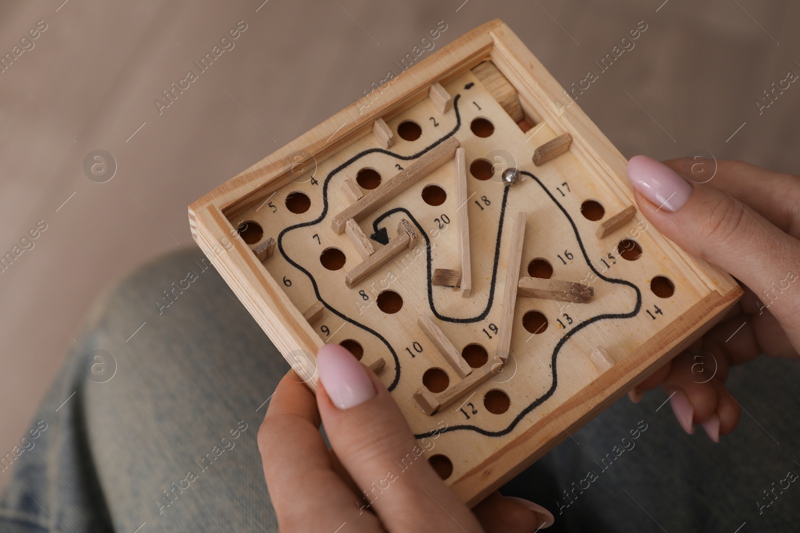 Photo of Woman holding wooden toy maze with metal ball on blurred background, closeup