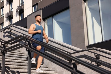 Photo of Happy man running down stairs outdoors on sunny day, low angle view. Space for text