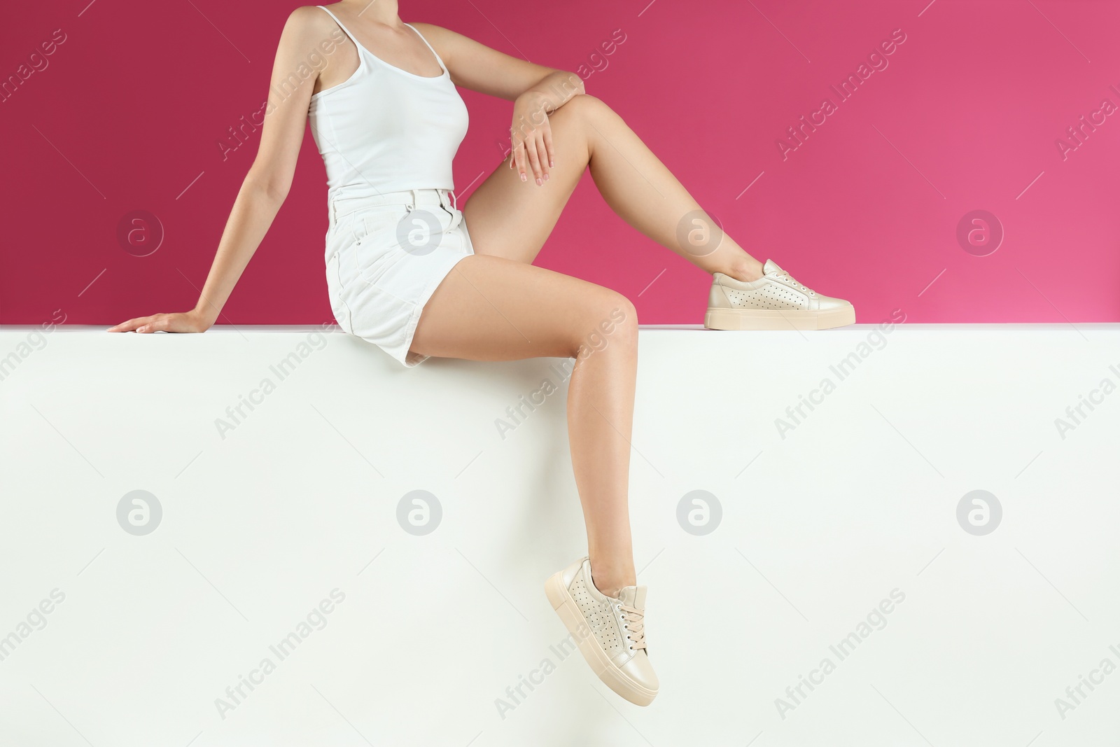 Photo of Woman in stylish shoes sitting on color background, closeup