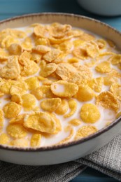 Photo of Bowl of tasty corn flakes on light blue wooden table, closeup