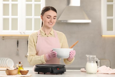 Young woman cooking delicious crepes in kitchen. Space for text