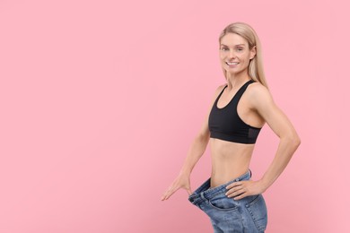 Photo of Slim woman wearing big jeans on pink background, space for text. Weight loss