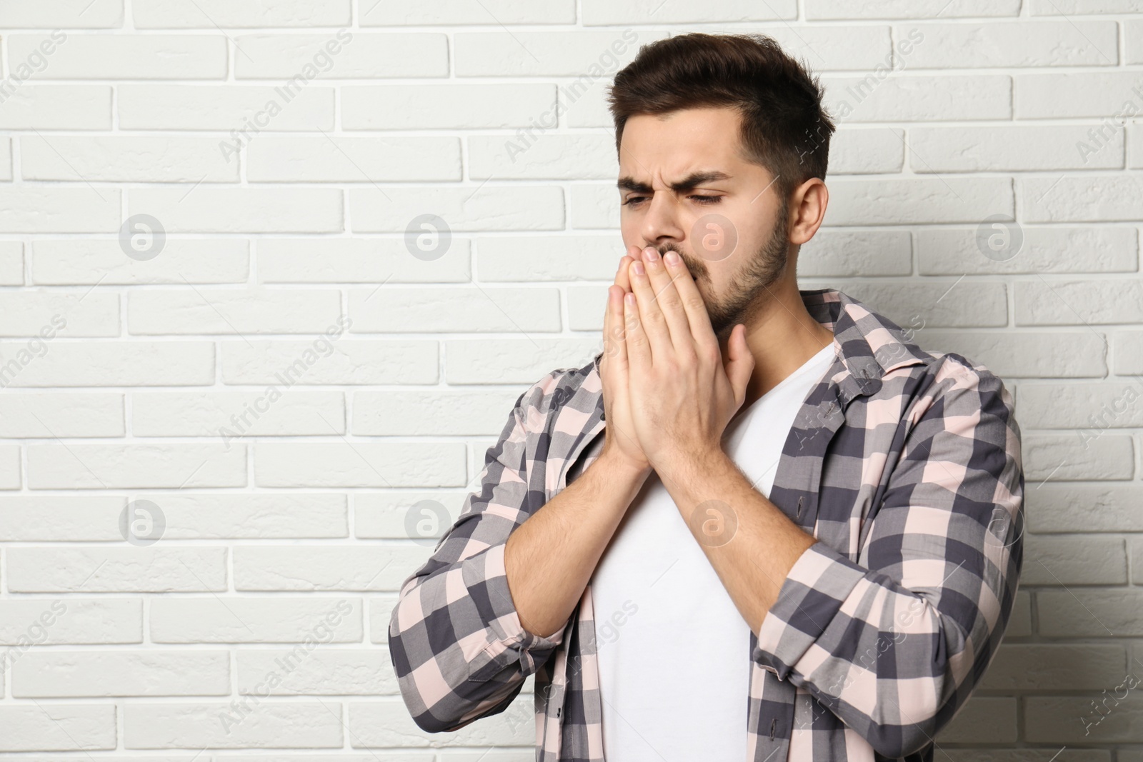 Photo of Handsome young man coughing near brick wall. Space for text