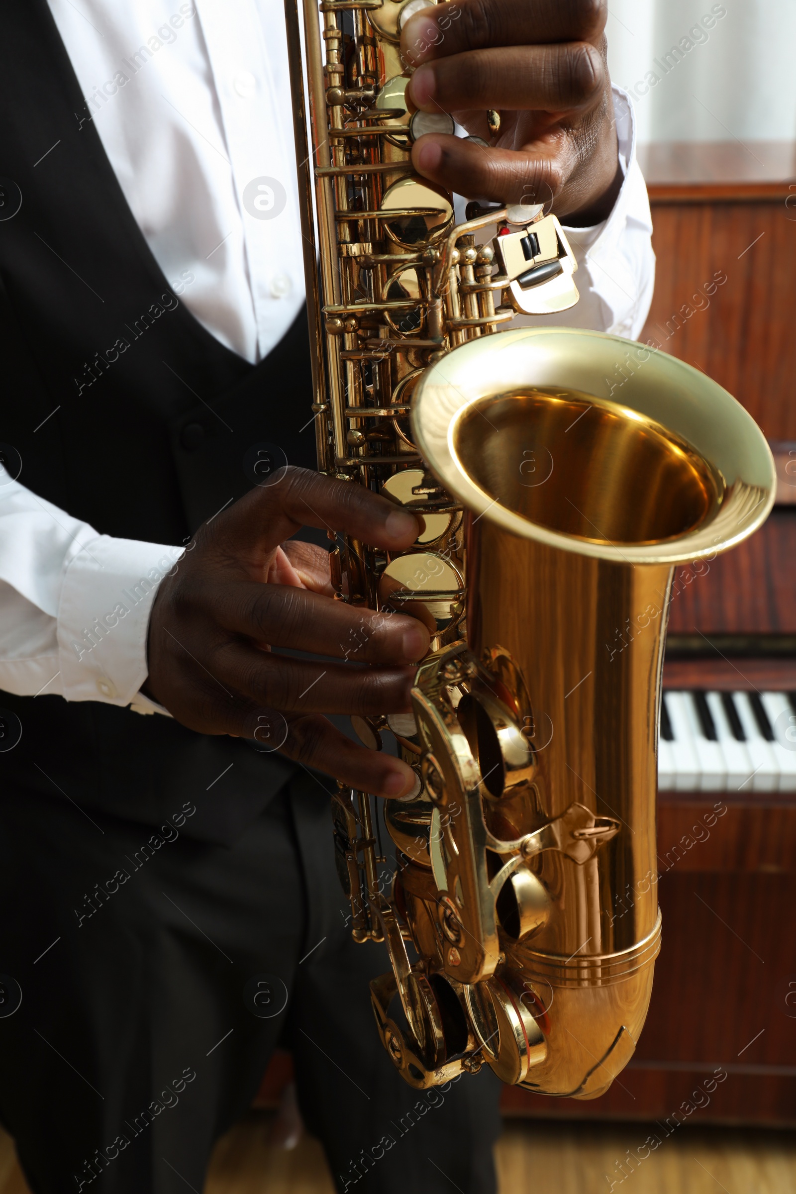 Photo of African-American man playing saxophone indoors, closeup. Talented musician