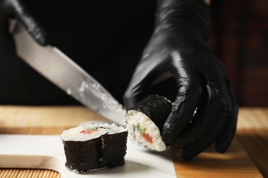 Chef in gloves cutting sushi roll at table, closeup