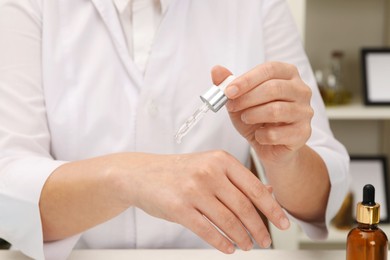 Dermatologist testing cosmetic product at table indoors, closeup