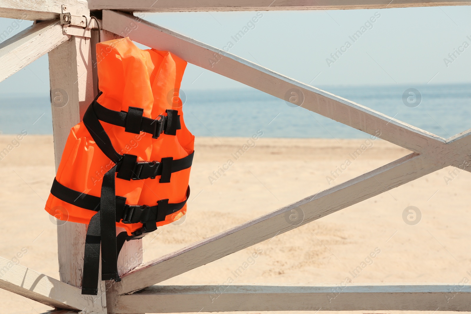 Photo of Orange life jacket hanging on wooden railing. Emergency rescue equipment