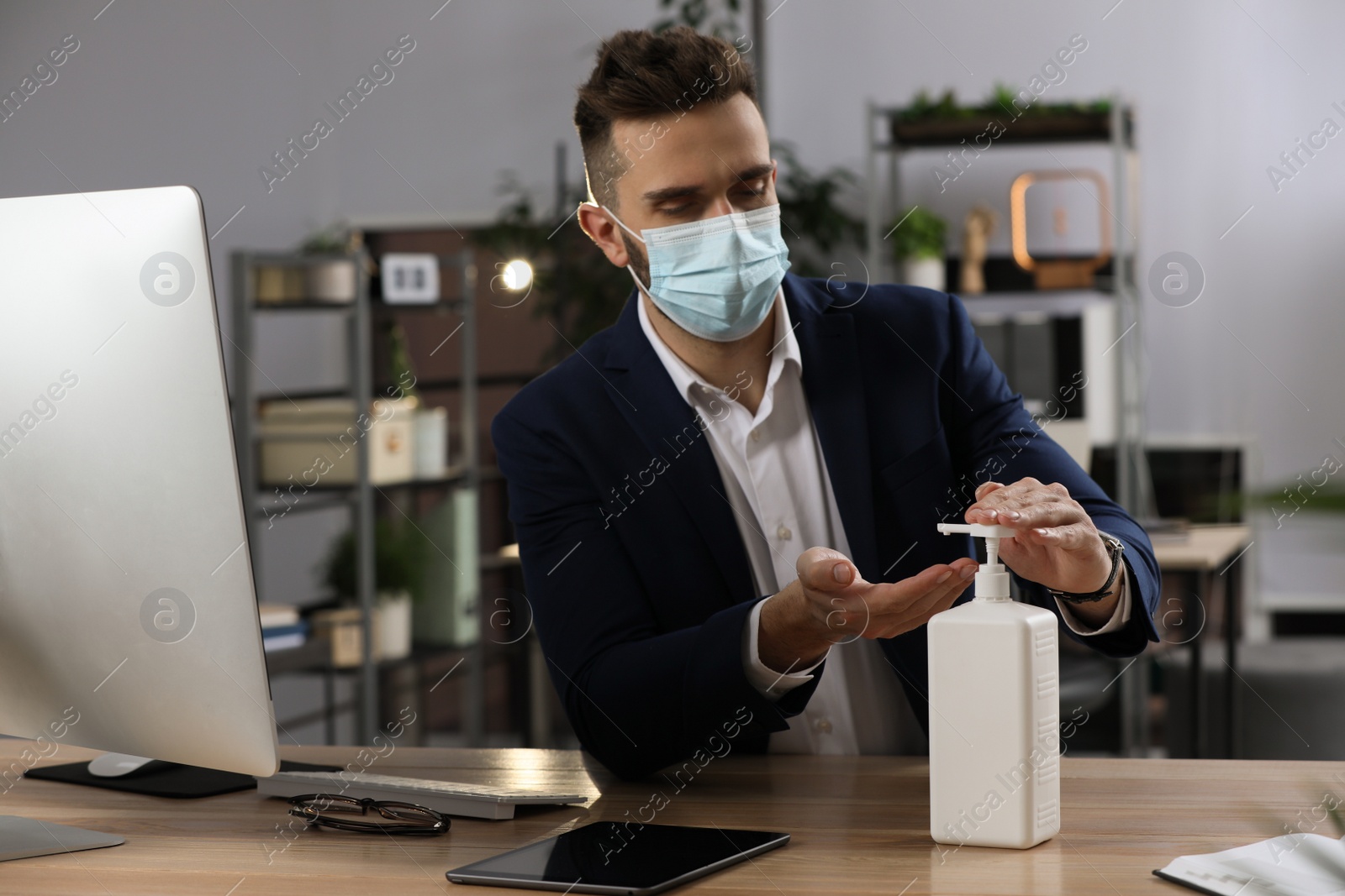 Photo of Man applying hand sanitizer at workplace in office. Personal hygiene during Coronavirus pandemic