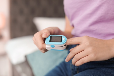 Photo of Young woman checking pulse with digital medical device indoors, closeup. Space for text