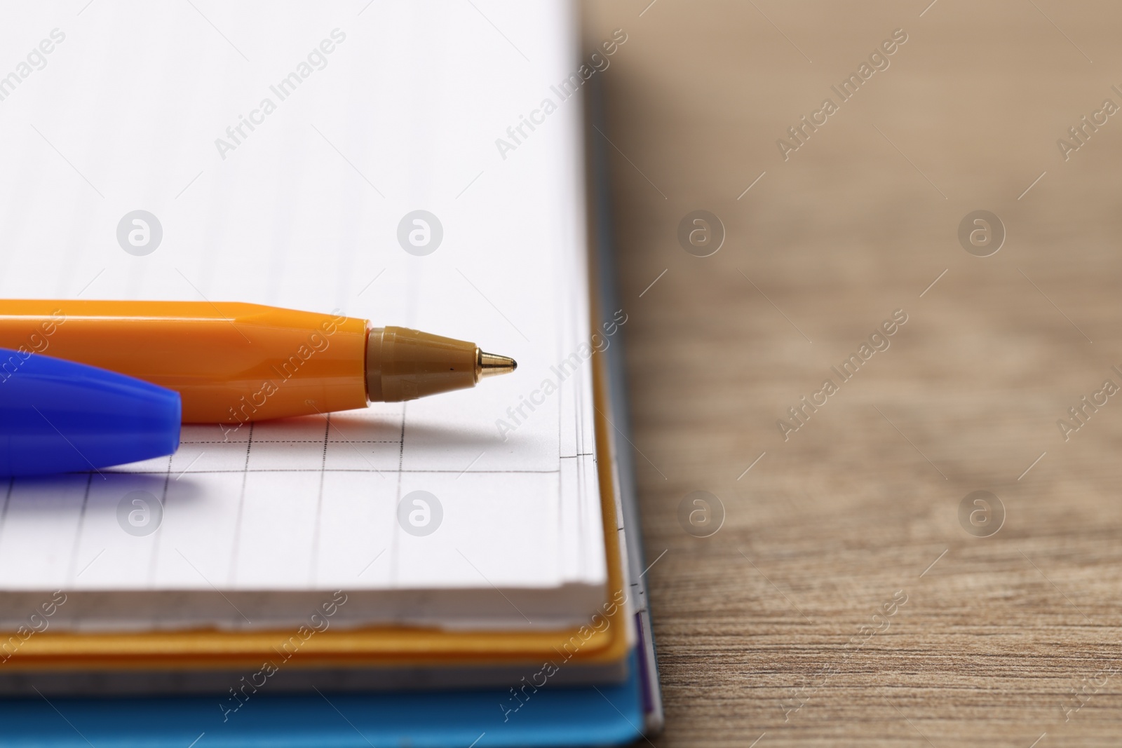 Photo of Ballpoint pen and notebook on wooden table, closeup. Space for text