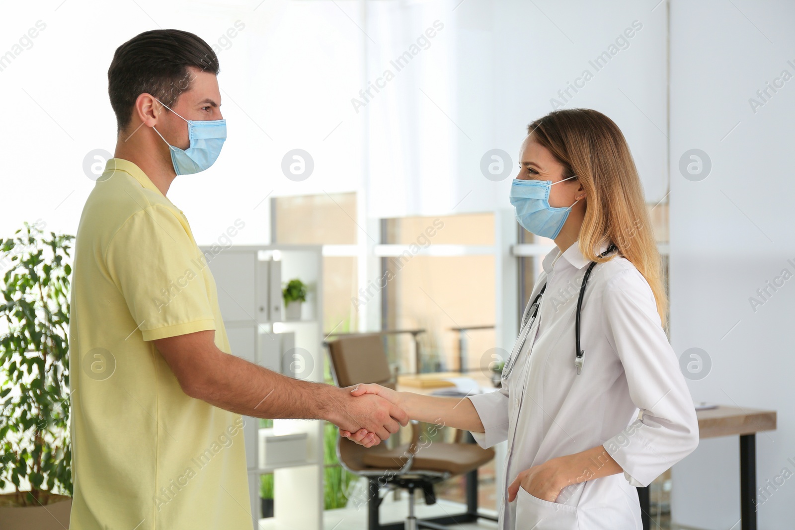 Photo of Doctor and patient in protective masks shaking hands indoors