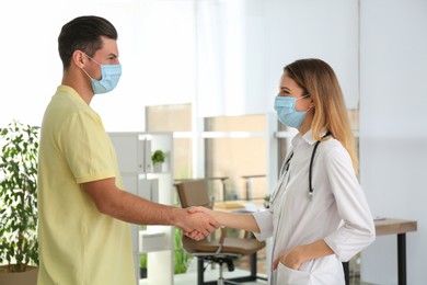 Doctor and patient in protective masks shaking hands indoors