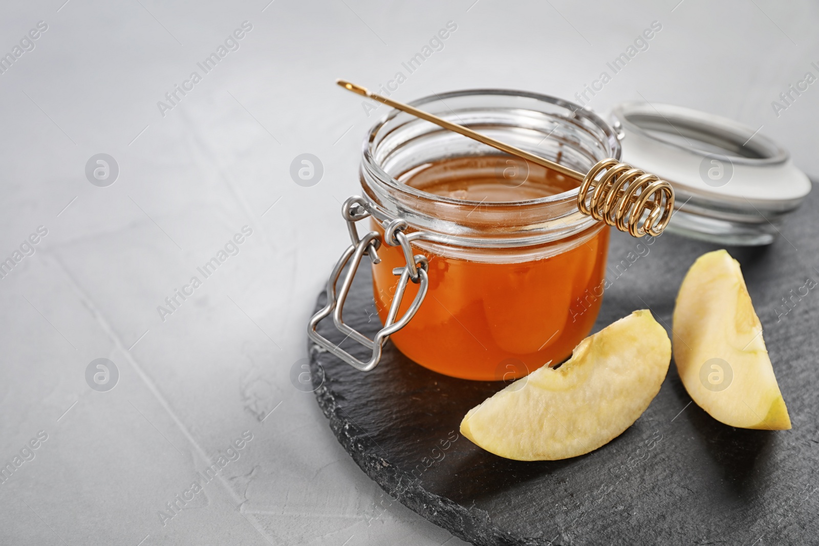 Photo of Slate plate with jar of honey, sliced apples and dipper on table