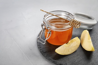 Slate plate with jar of honey, sliced apples and dipper on table