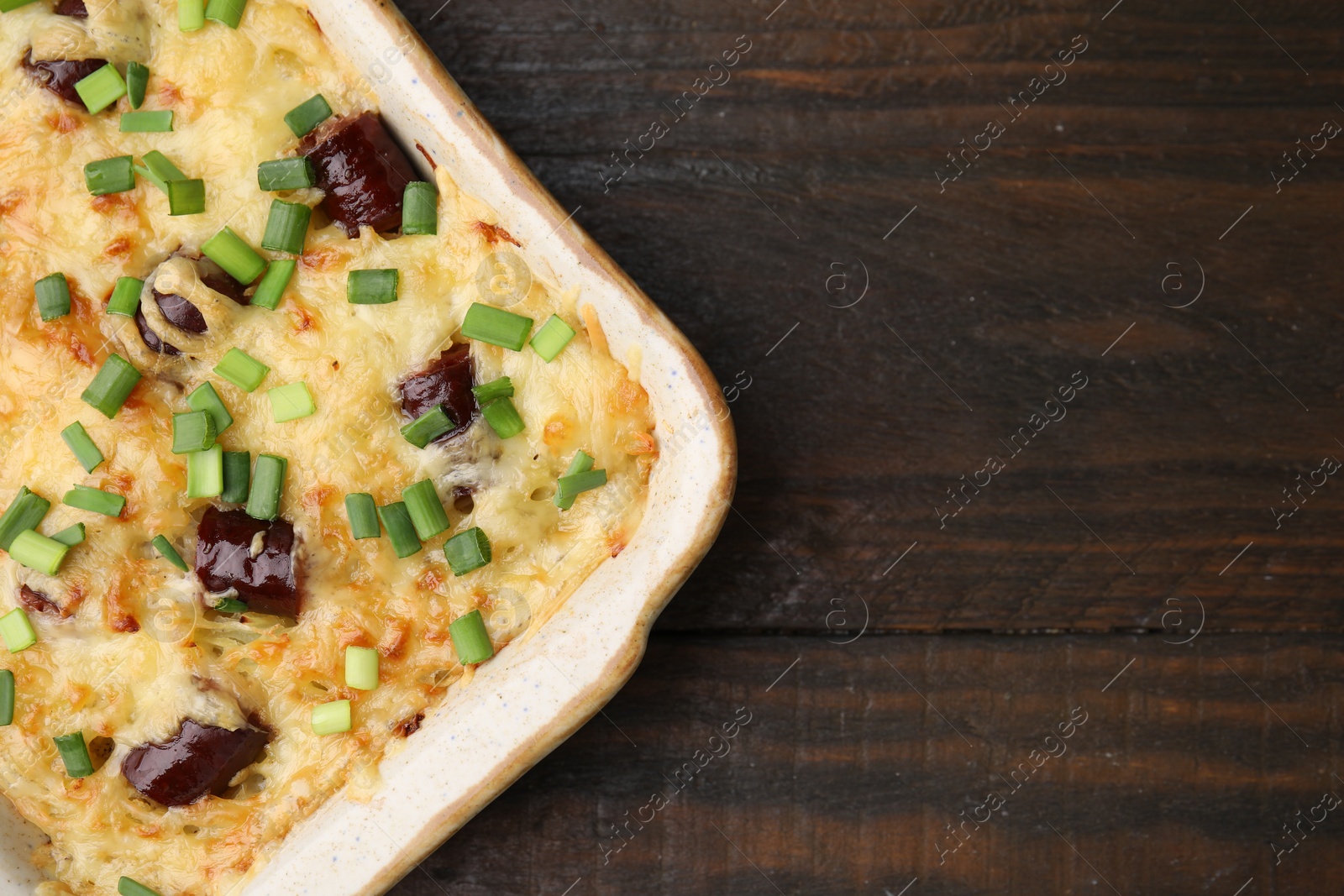 Photo of Tasty sausage casserole with green onions in baking dish on wooden table, top view. Space for text