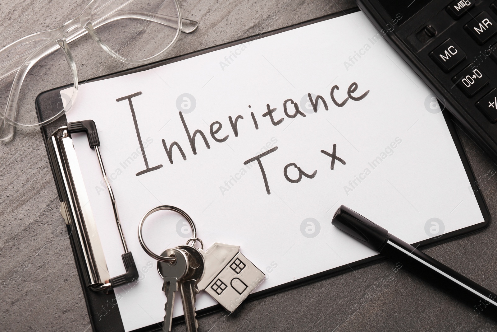 Photo of Inheritance Tax. Clipboard, marker, glasses and keys with key chain in shape of house on grey table