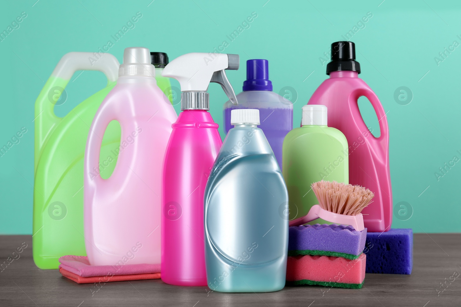 Photo of Different cleaning supplies and tools on wooden table against turquoise background