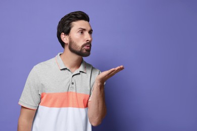 Photo of Handsome man blowing kiss on violet background. Space for text