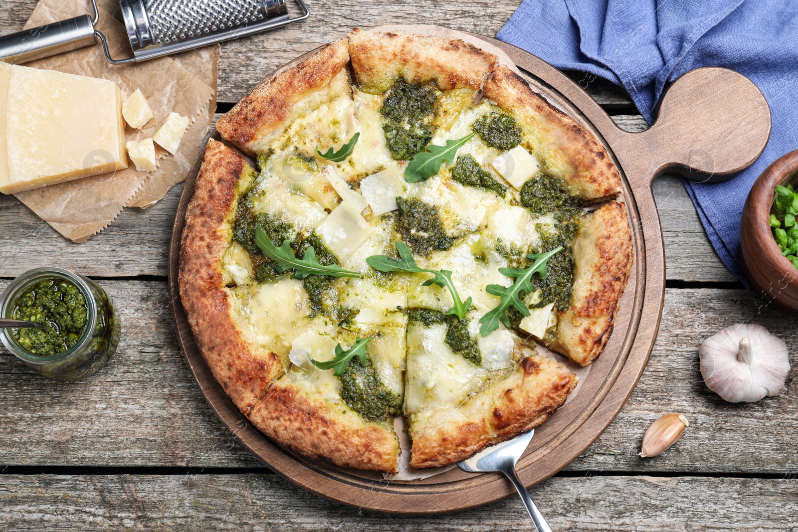 Photo of Delicious pizza with pesto, cheese and arugula served on wooden table, flat lay