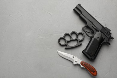 Photo of Black brass knuckles, gun and knife on light grey stone background, flat lay. Space for text