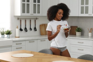 Beautiful woman in stylish underwear and t-shirt eating salad indoors, space for text