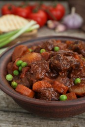 Photo of Delicious beef stew with carrots, peas and potatoes on wooden table, closeup