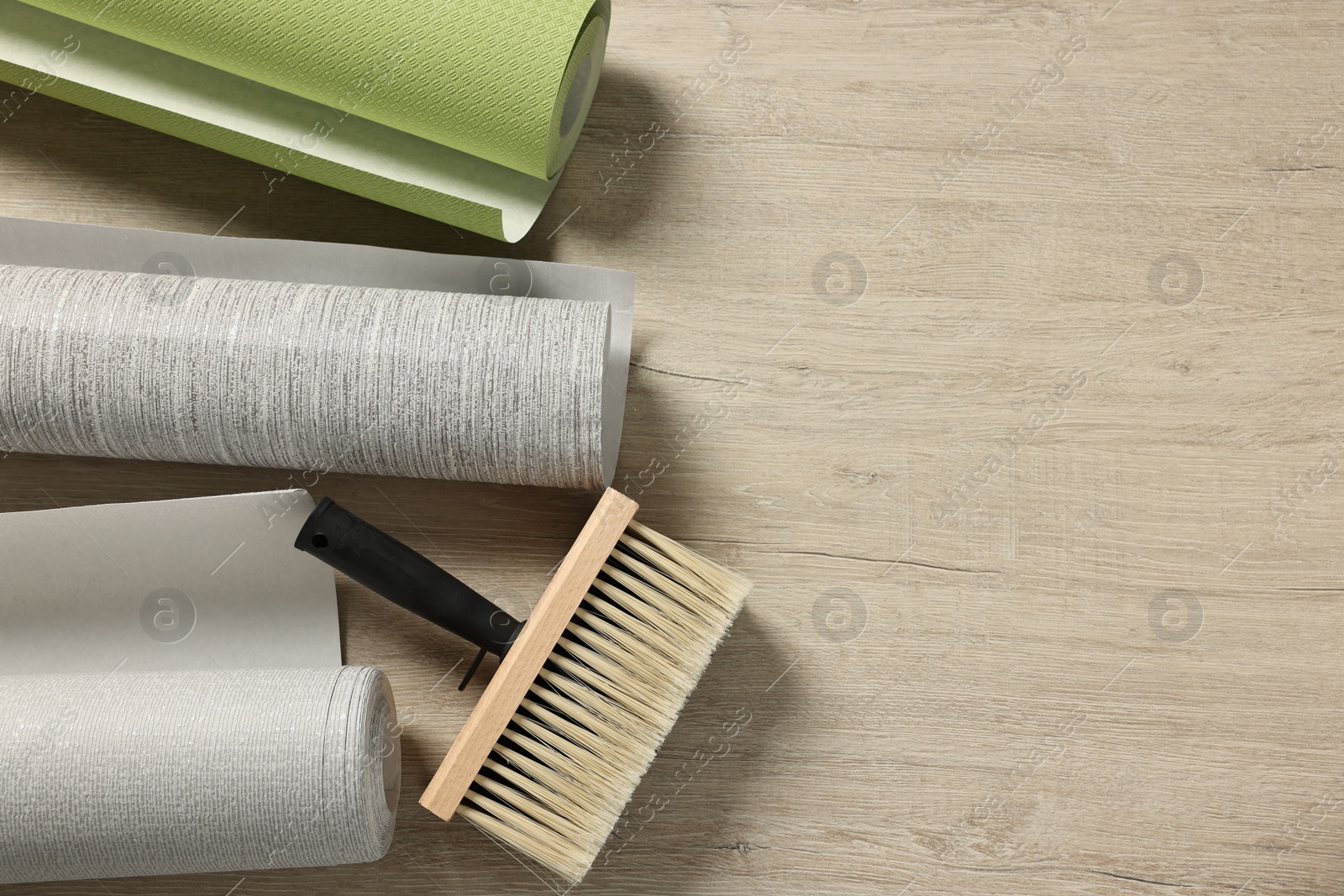 Photo of Different wallpaper rolls and brush on wooden table, flat lay. Space for text