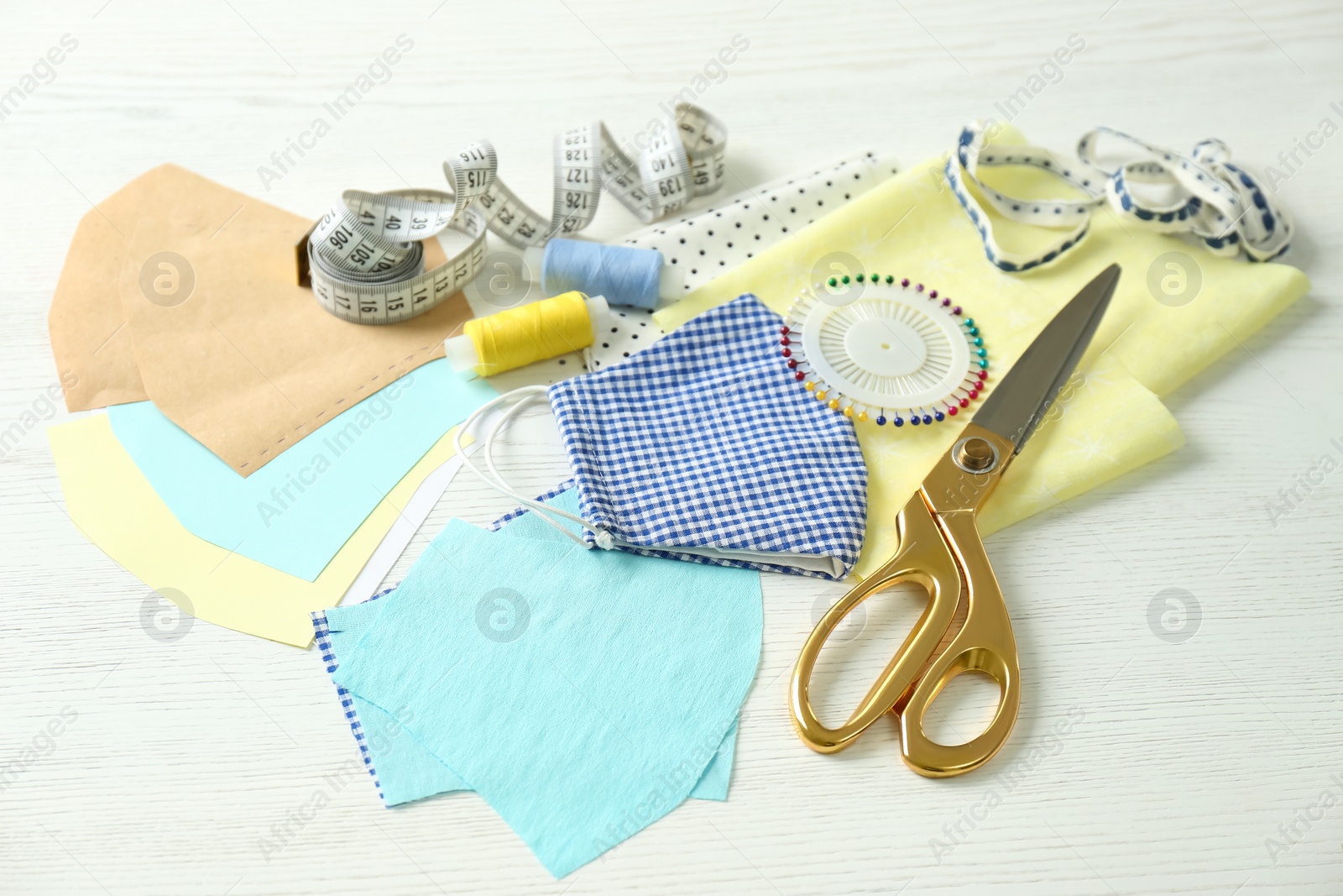 Photo of Fabric, sewing accessories and cloth mask on white wooden table. Personal protective equipment during COVID-19 pandemic