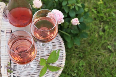 Photo of Glasses and bottle of delicious rose wine on picnic basket outdoors. Space for text