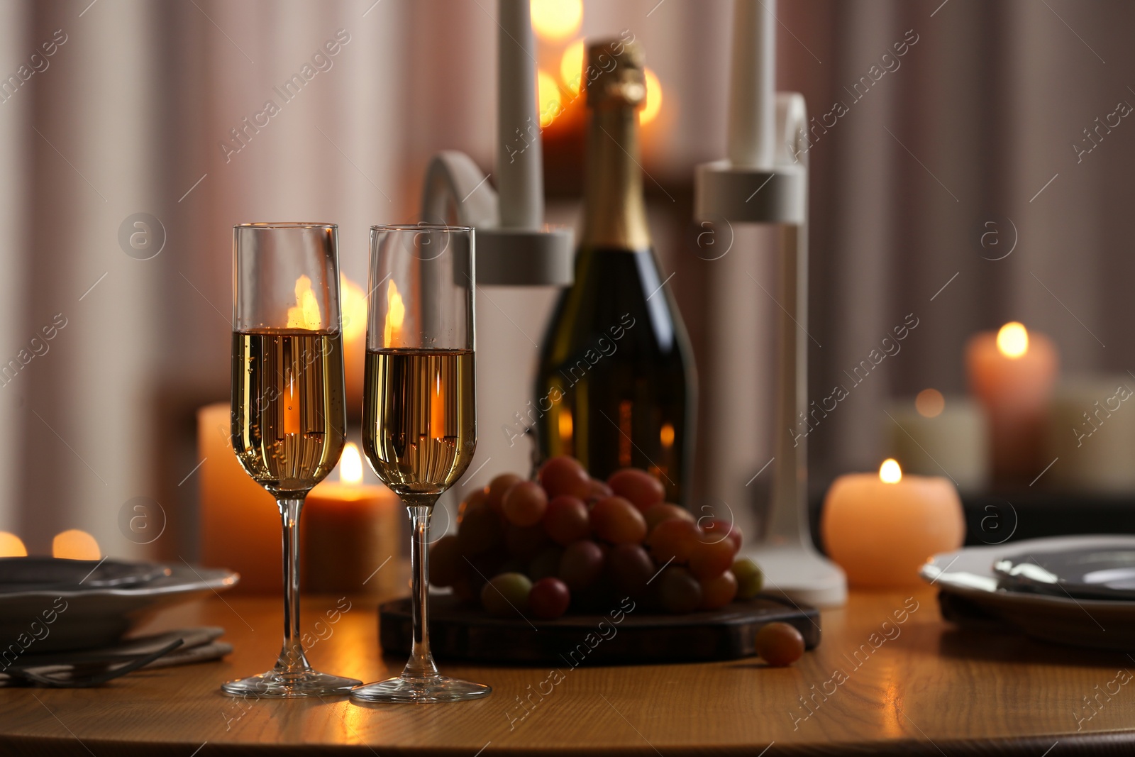 Photo of Glasses of champagne on wooden table against blurred burning candles