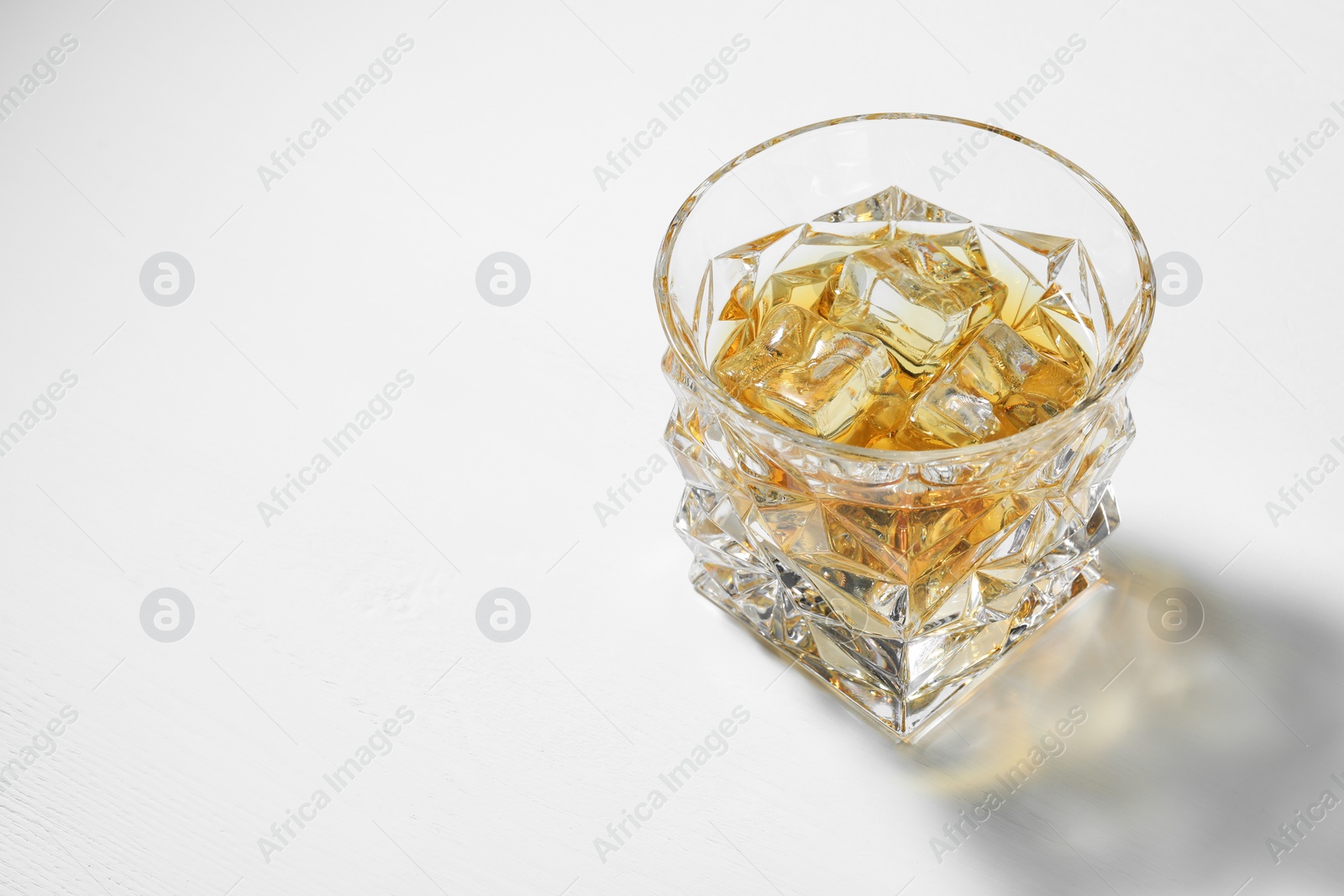 Photo of Whiskey with ice cubes in glass on white table, space for text