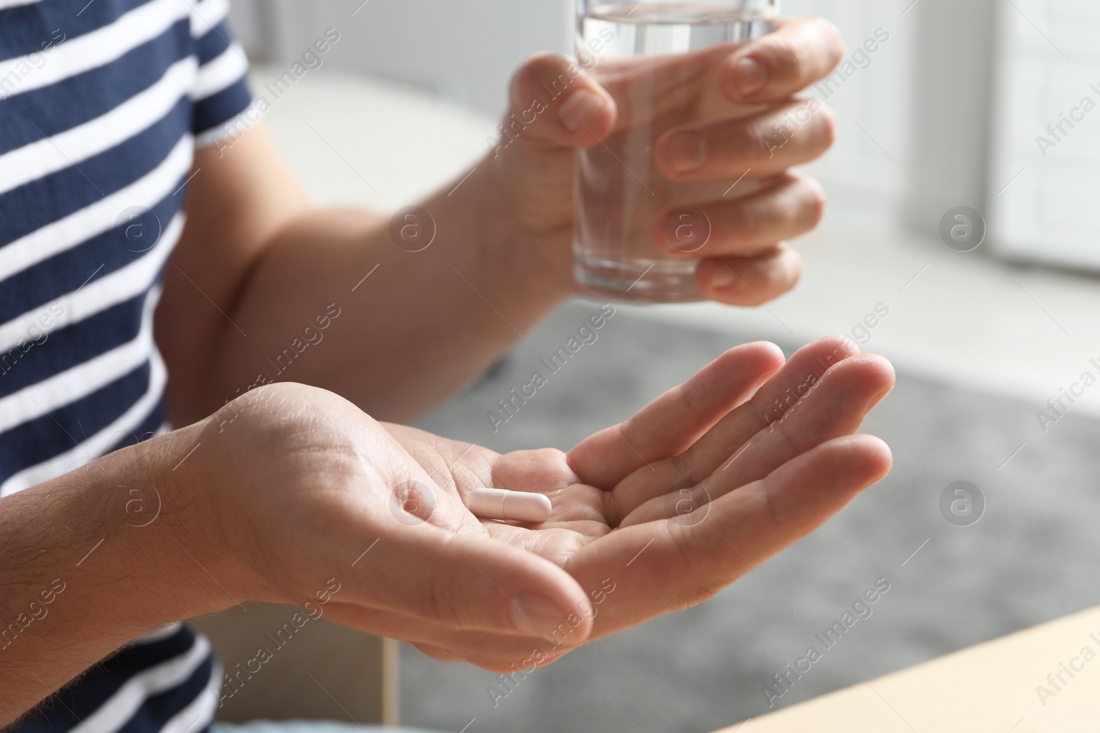 Photo of Man with glass of water and pill on blurred background, closeup