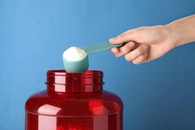 Photo of Man taking protein powder with scoop from jar against color background, closeup