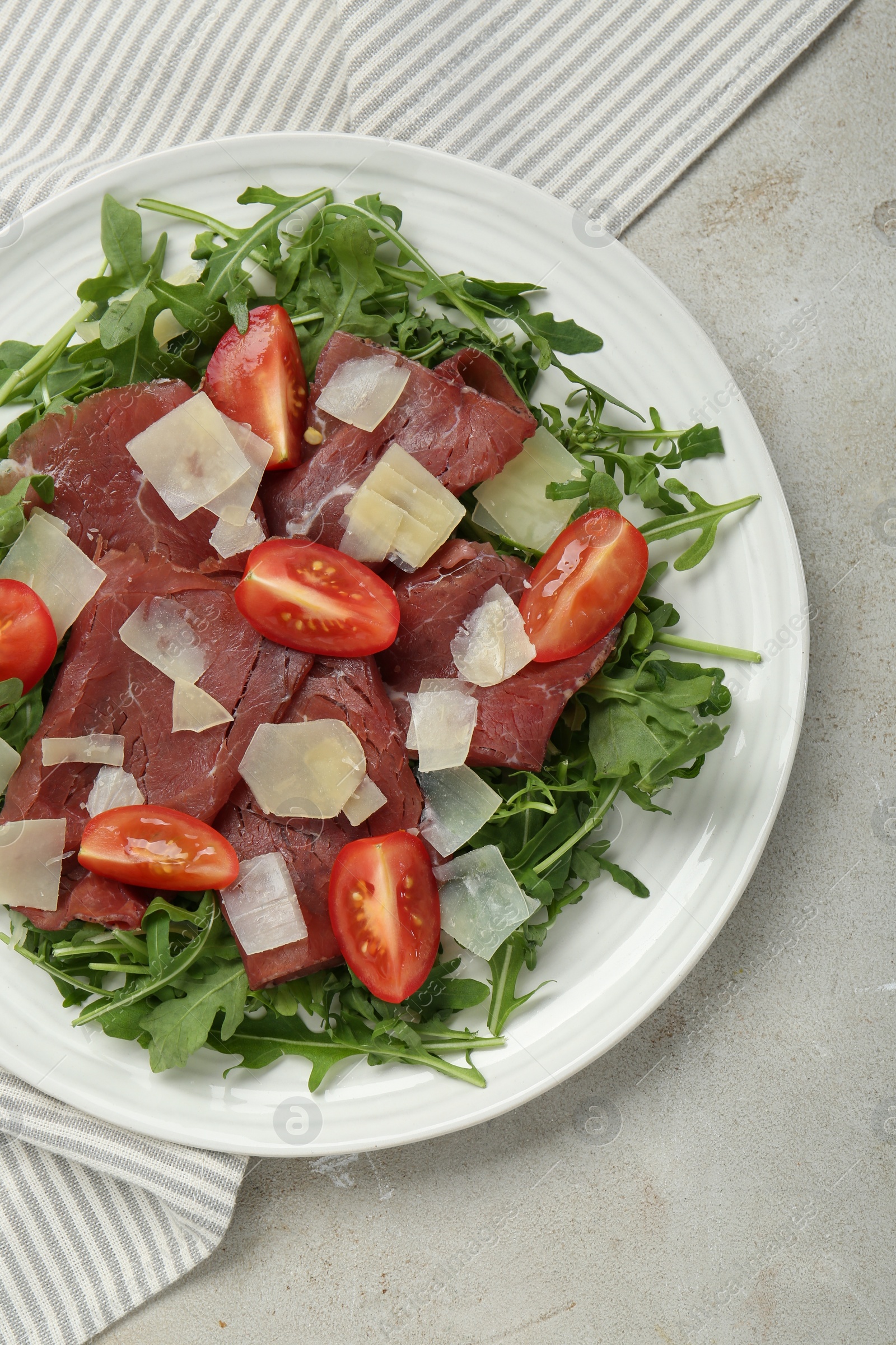 Photo of Delicious bresaola salad with parmesan cheese on light grey textured table, top view