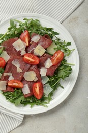 Photo of Delicious bresaola salad with parmesan cheese on light grey textured table, top view