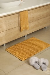 Photo of Soft orange bath mat and slippers on floor indoors