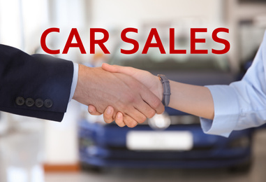 Image of Young salesman shaking hands with client in car dealership, closeup 