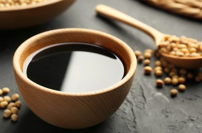 Tasty soy sauce in bowl and soybeans on black table, closeup