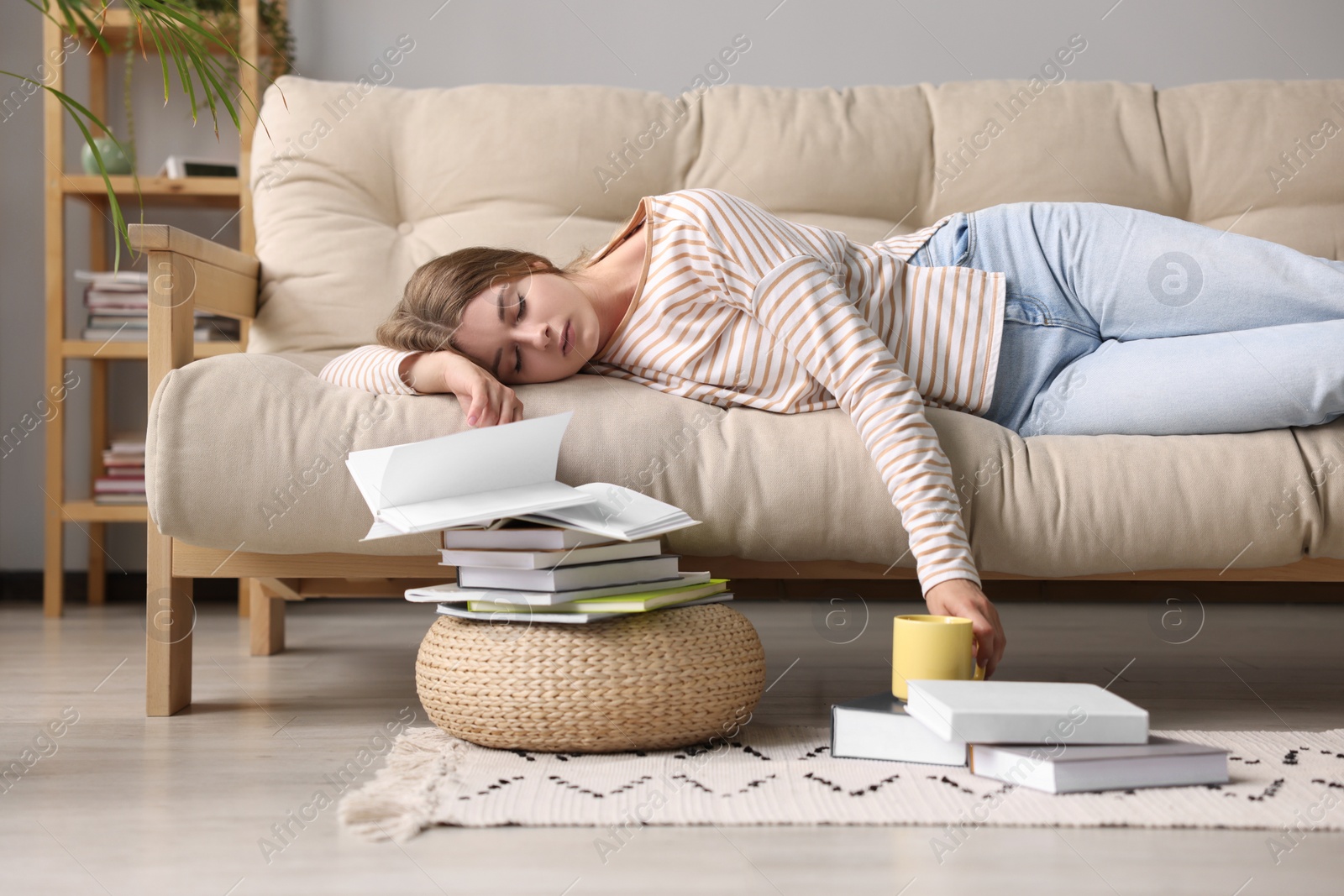 Photo of Young tired woman sleeping near books on couch at home