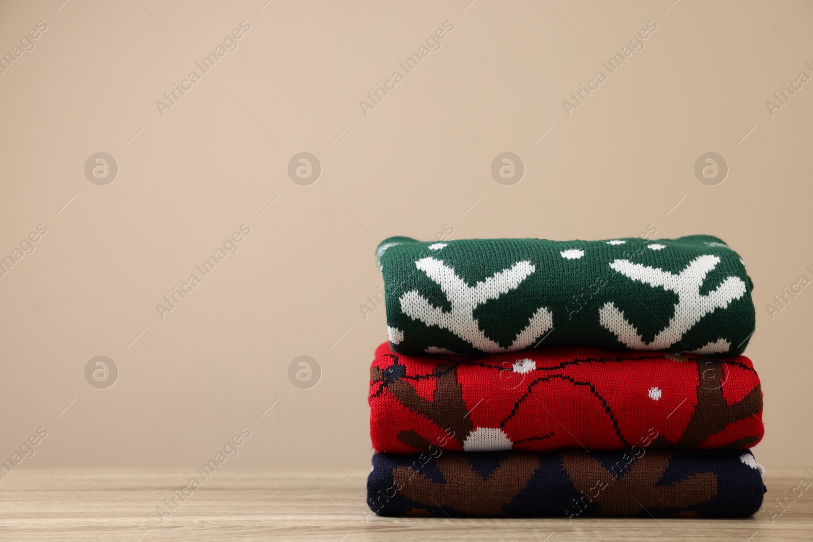 Photo of Stack of different Christmas sweaters on wooden table against beige background, space for text