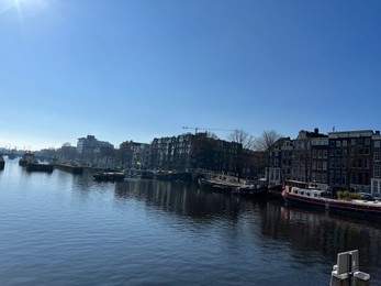 Amsterdam, Netherlands - March 01, 2023: Picturesque view of river embankment with moored boats in city under blue sky