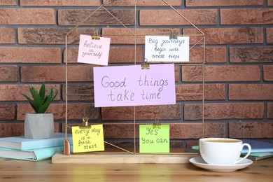 Photo of Notes with motivational quotes, coffee, houseplant and books on table against brick wall