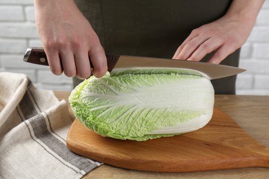 Photo of Woman cutting fresh Chinese cabbage at wooden table indoors, closeup