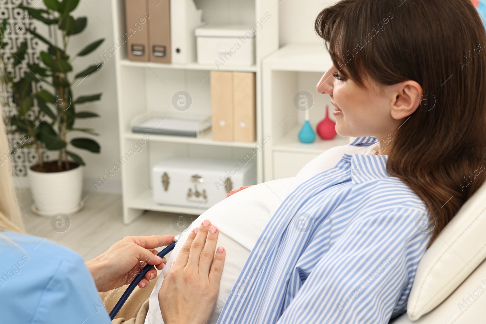 Photo of Pregnancy checkup. Doctor with stethoscope listening baby's heartbeat in patient's tummy in clinic, closeup